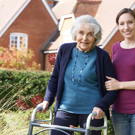 A senior with a walker heading outdoors with a younger woman
