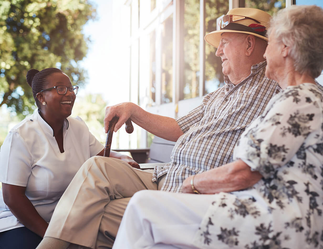 Seniors and a caregiver talking on a sunny porch